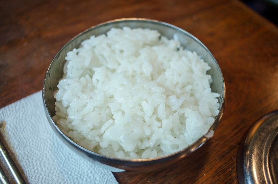 Arroz blanco cocido al vapor en un tazón de acero inoxidable sobre mesa de madera