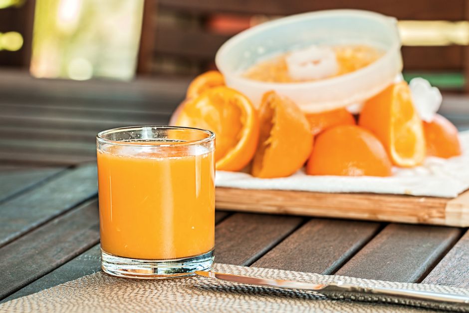 Vaso de jugo de naranja con naranjas rebanadas sobre mesa de madera